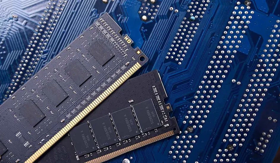 Two RAM sticks with gold contacts lie crossed on a blue circuit board filled with delicate traces and silver solder dots.