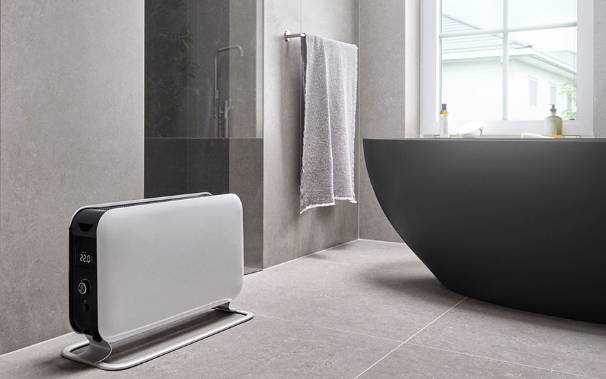 Een badkamer met grijze tegels, een radiator, een handdoek aan een rek en een zwart bad.