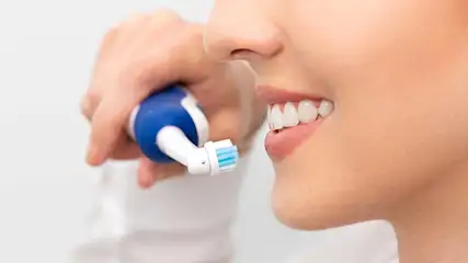 Brosse à dents électrique bleue et blanche près de dents blanches sur fond uni.