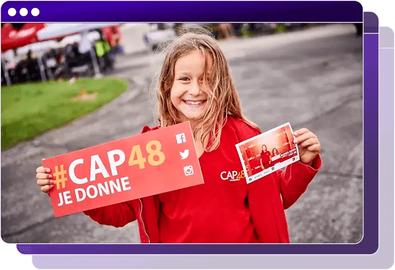 Personne portant un tee‑shirt rouge CAP48 tient une pancarte « #CAP48 JE DONNE » avec des icônes de réseaux sociaux et montre une petite photo, lors d’un événement en plein air.