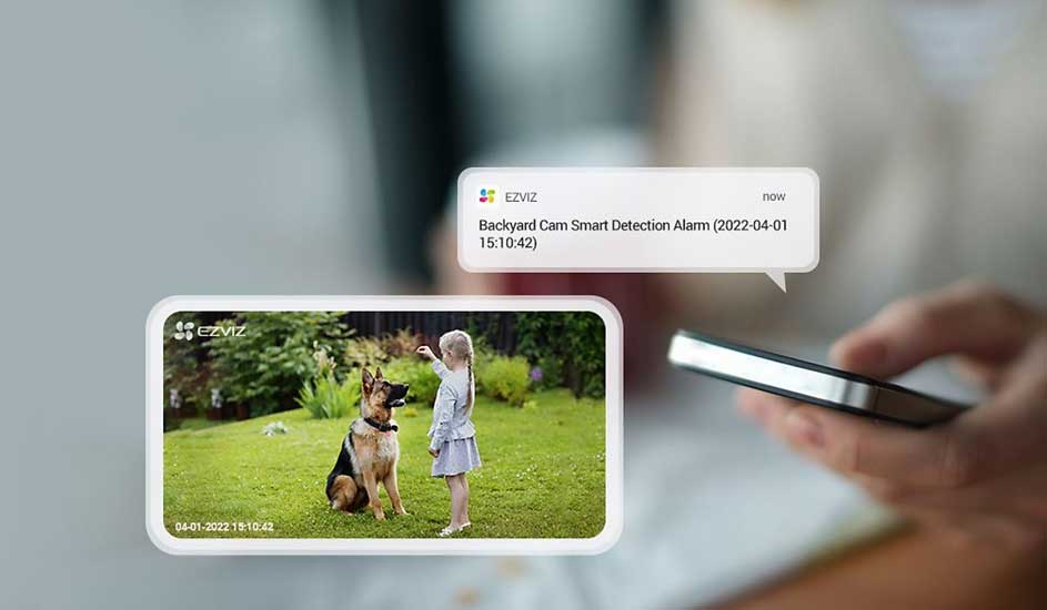 Op een smartphone verschijnt een EZVIZ-melding en camerabeeld van een meisje met een hond in de tuin. Alles is scherp en kleurrijk.