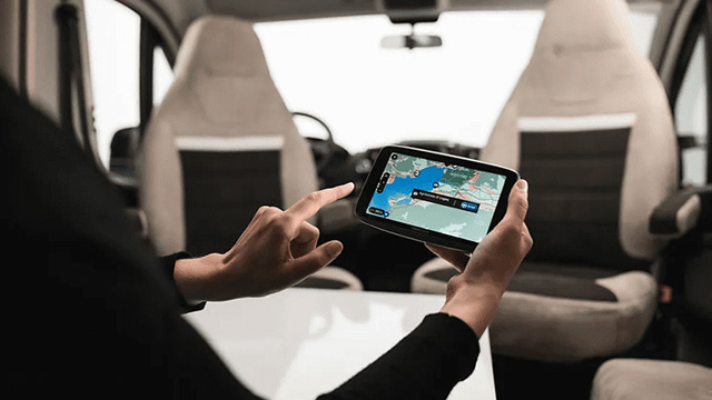 Une personne tient une tablette affichant une carte, dans un véhicule avec des sièges beiges et gris.