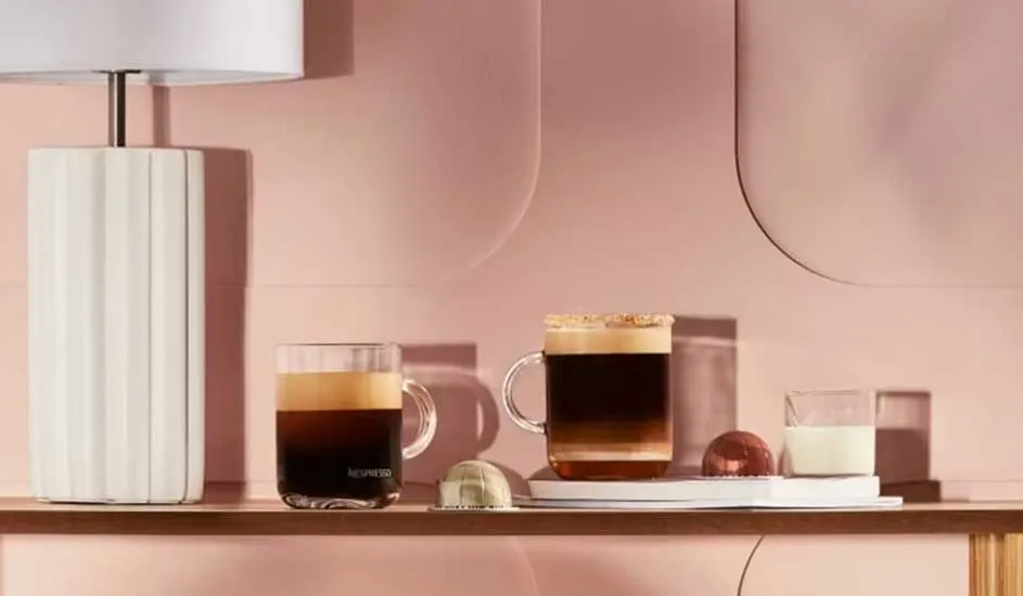 Twee glazen koffie, een glas melk en een lamp op een roze achtergrond.