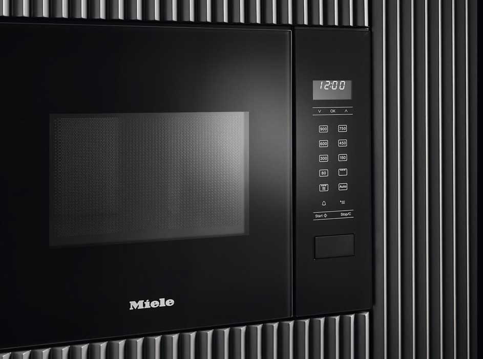 Zwarte Miele microgolfoven met digitaal display en knoppen, ingebouwd in een wand met verticale ribbels.