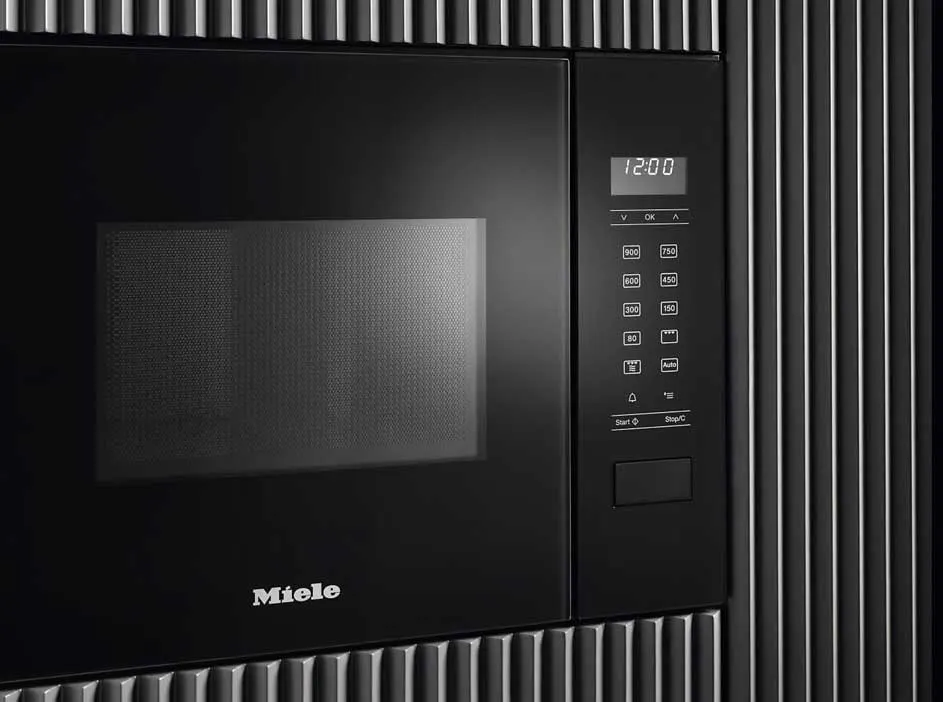 Zwarte Miele microgolfoven met digitaal display en knoppen, ingebouwd in een wand met verticale ribbels.