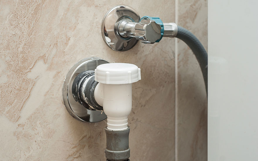 Deux robinets chromés sont fixés au mur beige. Le robinet supérieur a une poignée bleue et un tuyau gris. Le robinet inférieur est blanc.