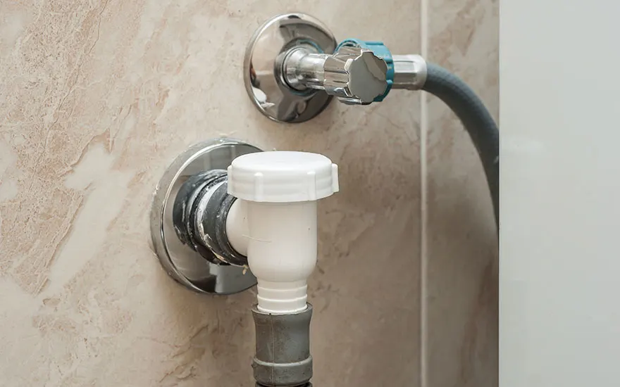 Deux robinets chromés sont fixés au mur beige. Le robinet supérieur a une poignée bleue et un tuyau gris. Le robinet inférieur est blanc.