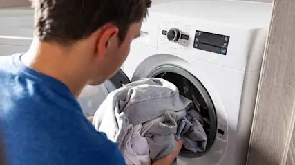 Een witte wasmachine met open deur, gevuld met grijze kleding.