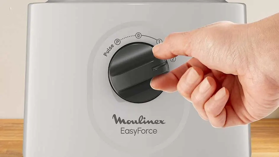 Gros plan d'un mixeur Moulinex EasyForce blanc avec une main ajustant le cadran de vitesse noir.