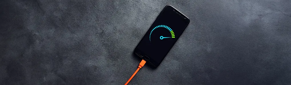 Un smartphone noir est branché sur un câble orange sur un fond gris foncé. L'écran affiche un indicateur de vitesse bleu et vert.