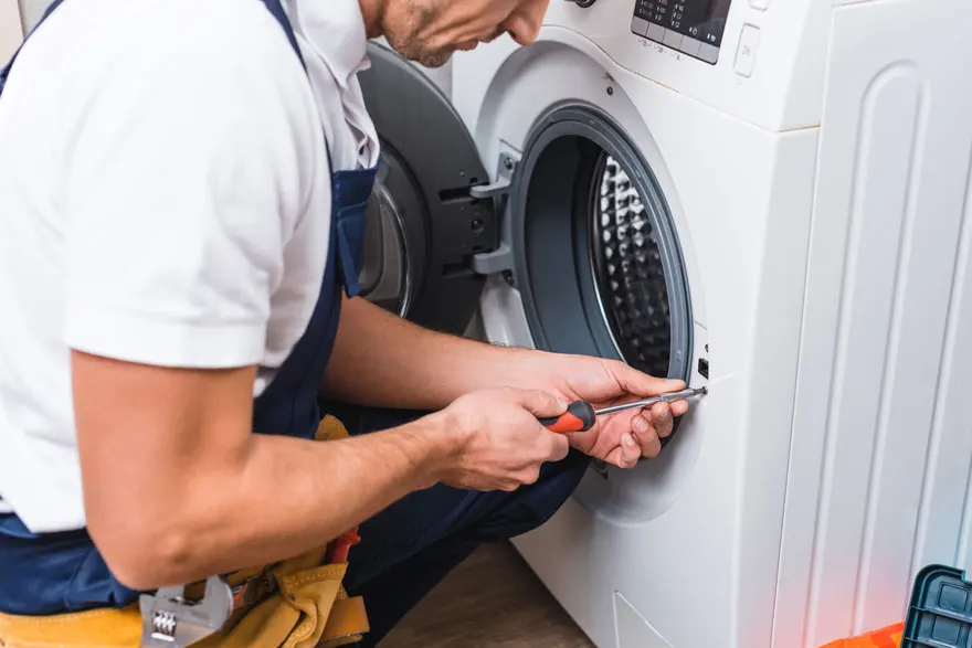 Een witte wasmachine met open deur wordt gerepareerd met een schroevendraaier.