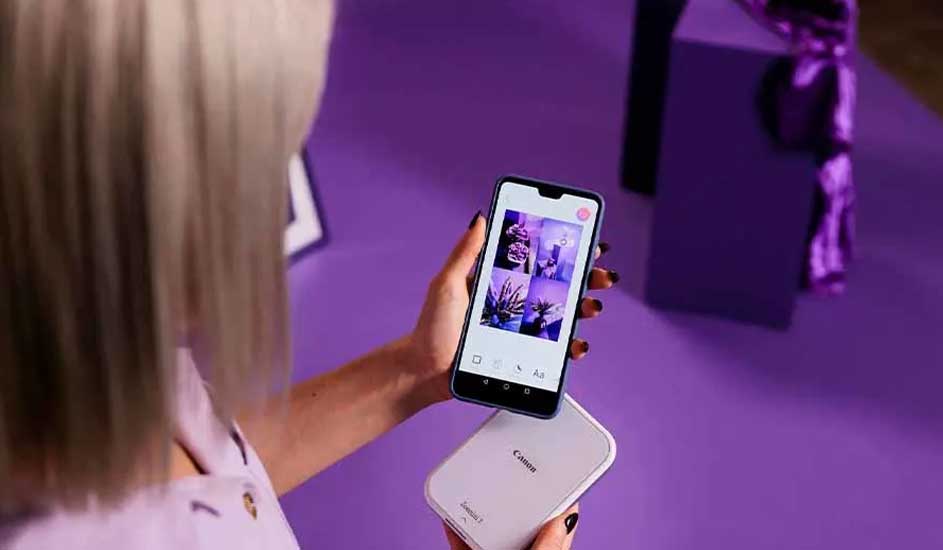Een smartphone toont foto's bovenop een witte Canon printer, tegen een paarse achtergrond.