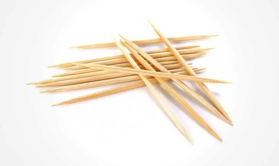 Een stapel houten tandenstokers ligt verspreid op een witte achtergrond.