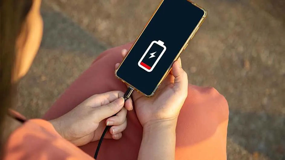 Een telefoon met een bijna lege batterij wordt opgeladen. Het scherm toont een rode batterij-indicator met een bliksemschicht.