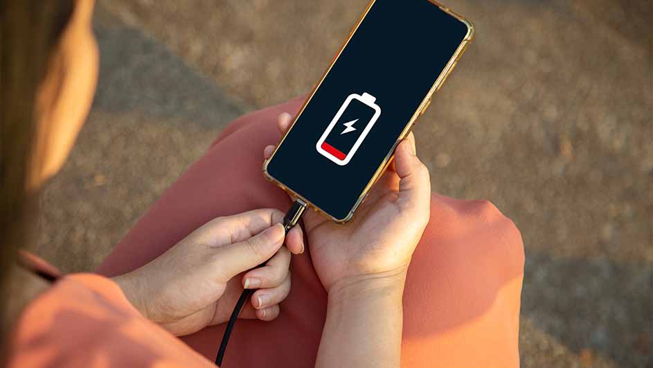 Téléphone doré branché, affichant une batterie faible avec un éclair rouge sur un écran noir. Câble noir connecté.