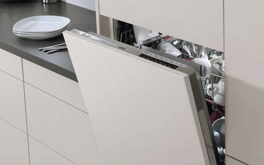 Un lave-vaisselle blanc est entrouvert dans une cuisine moderne. Vaisselle propre visible à l'intérieur. Assiettes sur le comptoir gris.