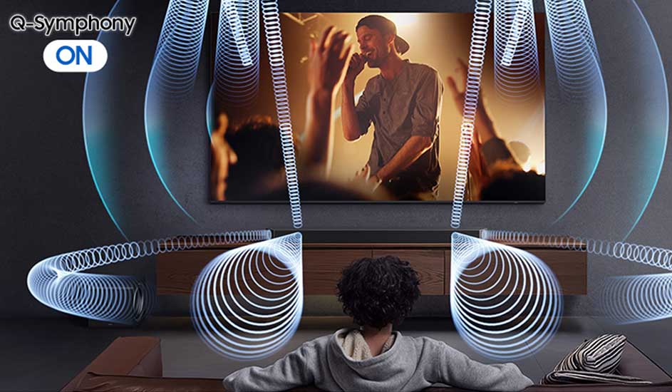 Een persoon kijkt naar een Samsung televisie met Q-Symphony aan, terwijl geluidsgolven van de soundbar en tv een meeslepende muziekervaring tonen.