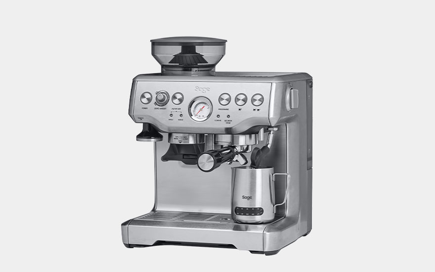 A coffee maker, white and black, dispenses a layered coffee drink into a clear glass mug on a gray background.