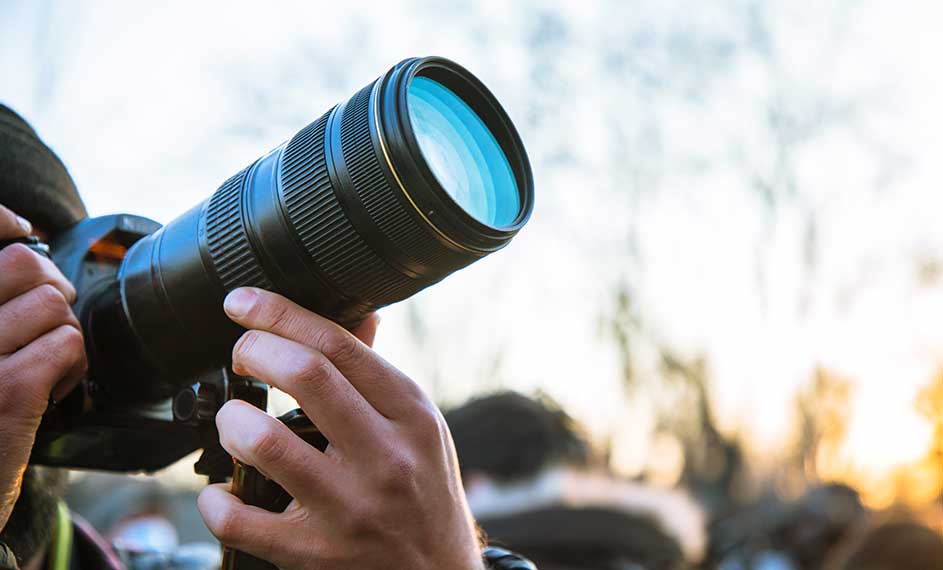 Een zwarte camera met een blauwe lens wordt vastgehouden tegen een vage achtergrond van de lucht.
