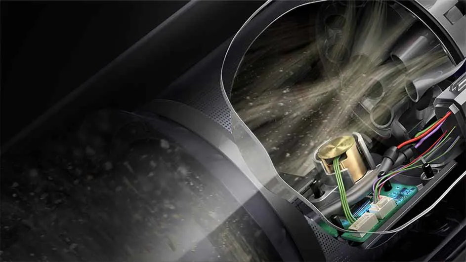 Vue en coupe d'un aspirateur gris foncé avec des fils colorés et un circuit imprimé vert. De la poussière est visible à l'intérieur.