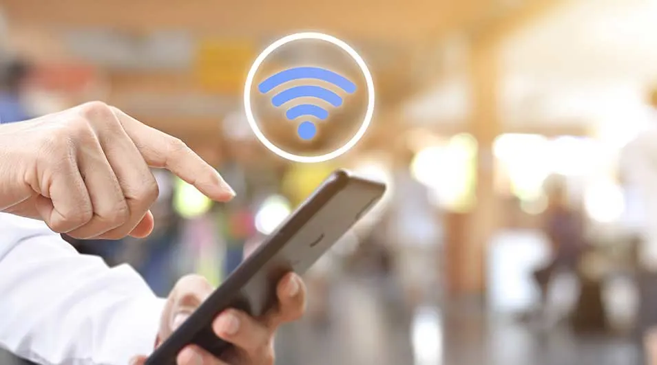 Main tenant un smartphone noir avec une icône Wi-Fi bleue. Arrière-plan flou.