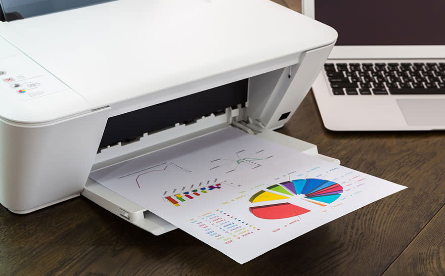 Imprimante blanche avec feuille imprimée de diagrammes et ordinateur portable sur une table en bois.