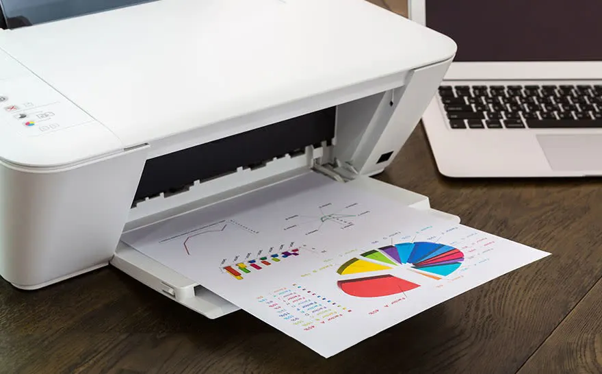 Imprimante blanche avec feuille imprimée de diagrammes et ordinateur portable sur une table en bois.