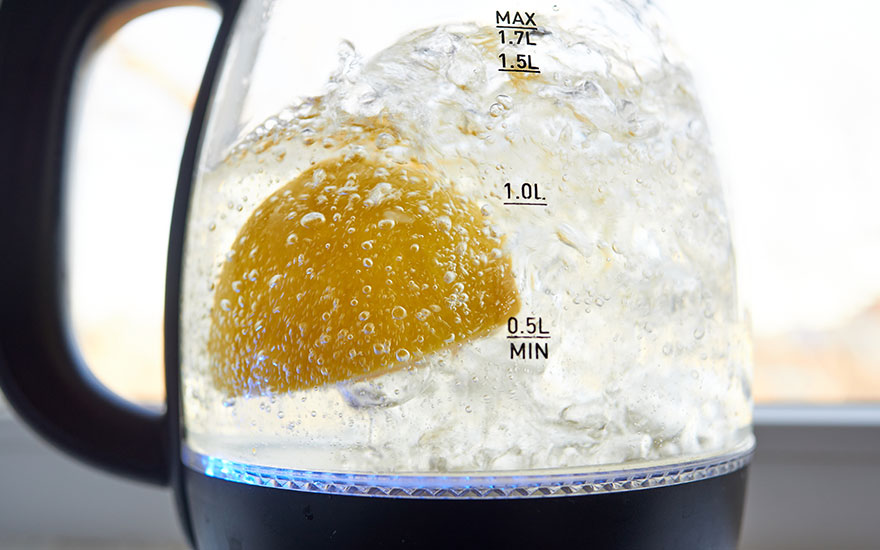 Une bouilloire en verre chauffe de l'eau avec un citron. L'eau bouillonne autour du fruit jaune.