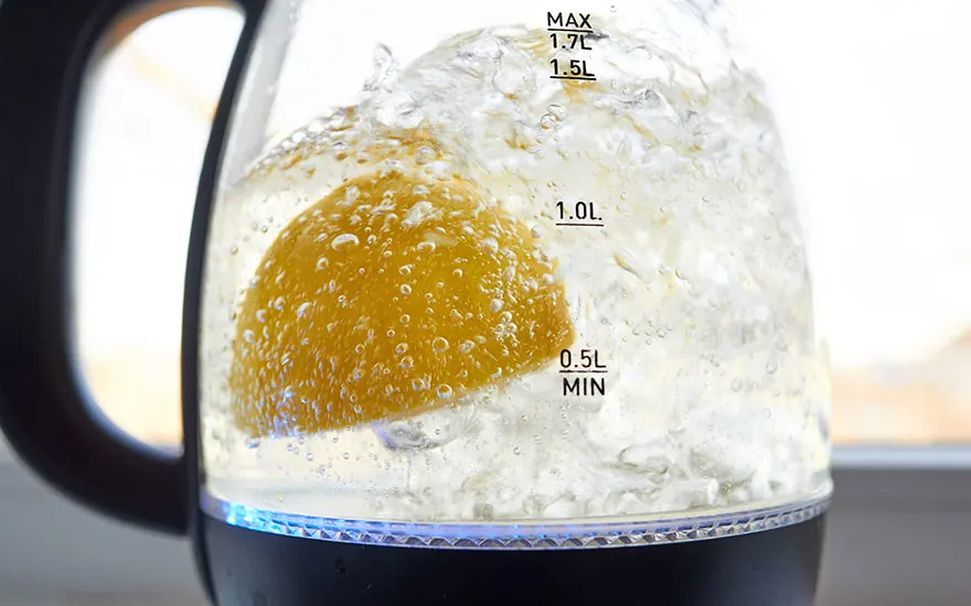 Une bouilloire en verre chauffe de l'eau avec un citron. L'eau bouillonne autour du fruit jaune.