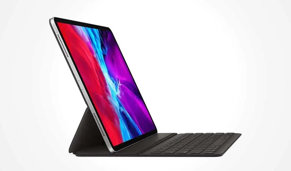 Un iPad avec un écran allumé est fixé sur un clavier noir sur fond blanc. L'écran affiche des couleurs vives.
