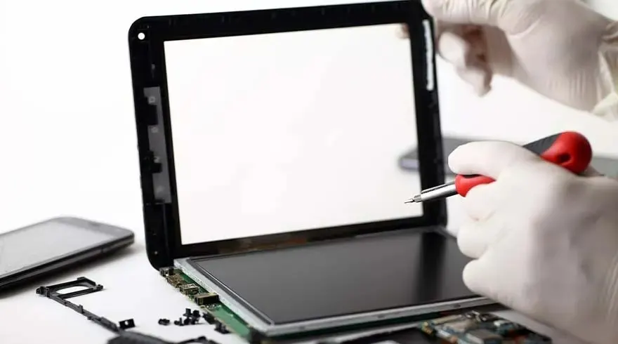 Un écran de tablette noir est en réparation avec un tournevis rouge, sur un fond blanc.
