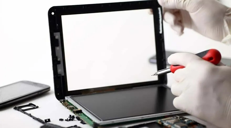 Een tablet wordt gerepareerd met een schroevendraaier. Er liggen onderdelen en een smartphone op de witte achtergrond.