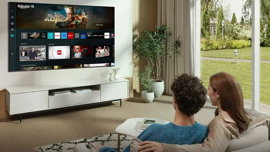Woonkamer met tv waarop Rakuten TV menu getoond wordt. Een witte tv-meubel staat eronder. Buiten is een tuin te zien.