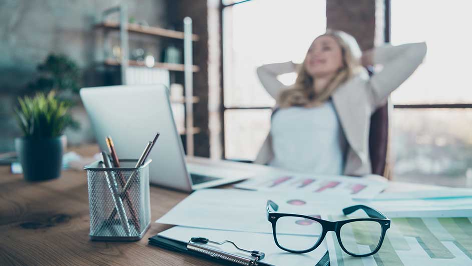 Bureau avec ordinateur portable, lunettes, documents et pot à crayons. Une plante verte est également visible.