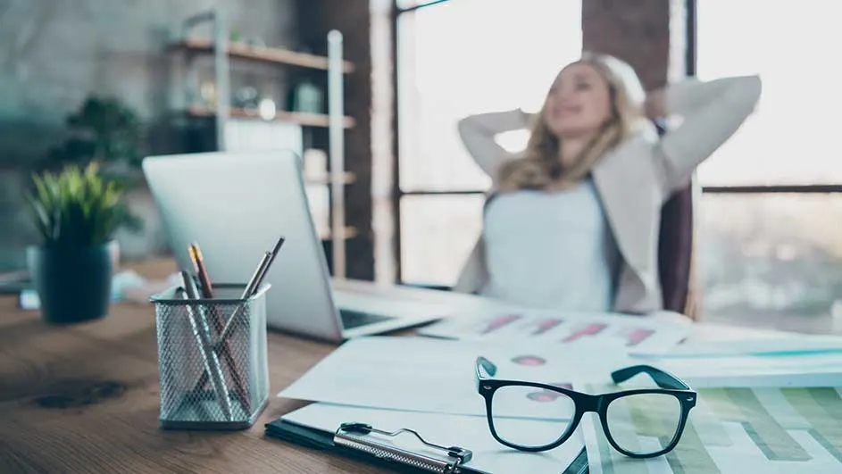 Bureau avec ordinateur portable, lunettes, documents et pot à crayons. Une plante verte est également visible.