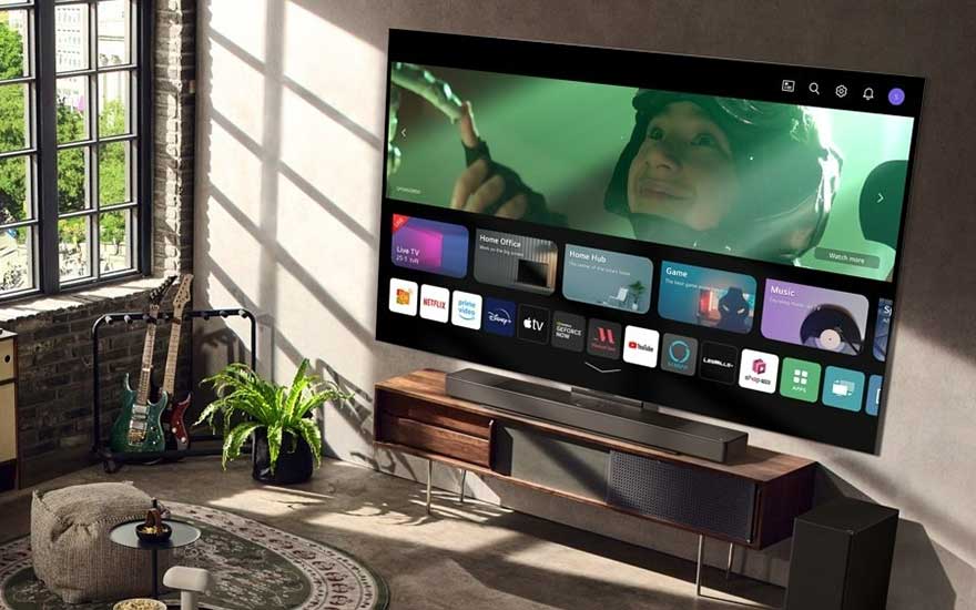 Un grand écran de télévision affiche un menu d'applications. Sous l'écran se trouve un meuble en bois et une barre de son.