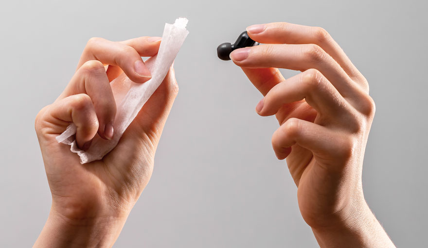 Deux mains tiennent un écouteur noir et un tissu blanc sur fond gris.