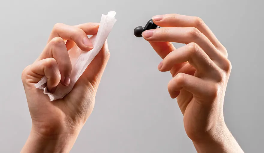 Deux mains tiennent un écouteur noir et un tissu blanc sur fond gris.