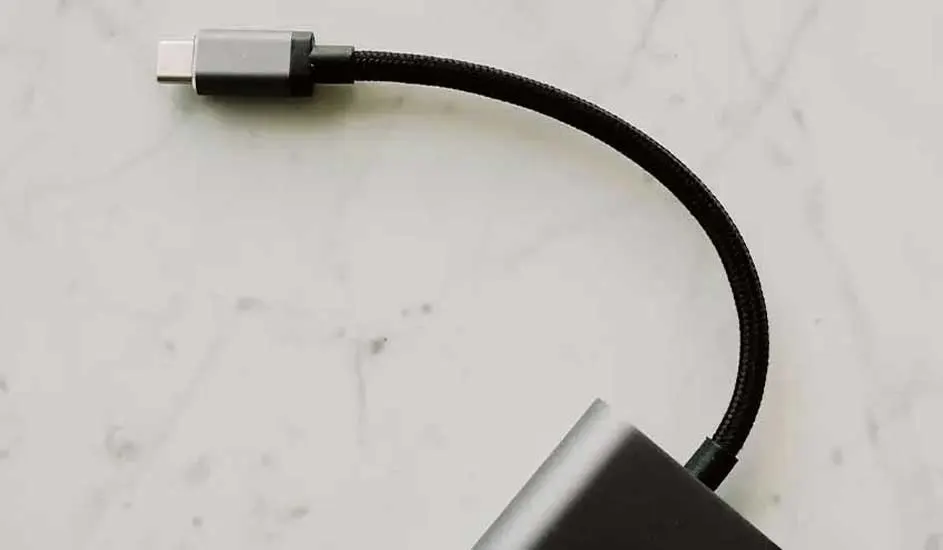 Un câble USB-C noir est connecté à un adaptateur gris sur une surface blanche marbrée.