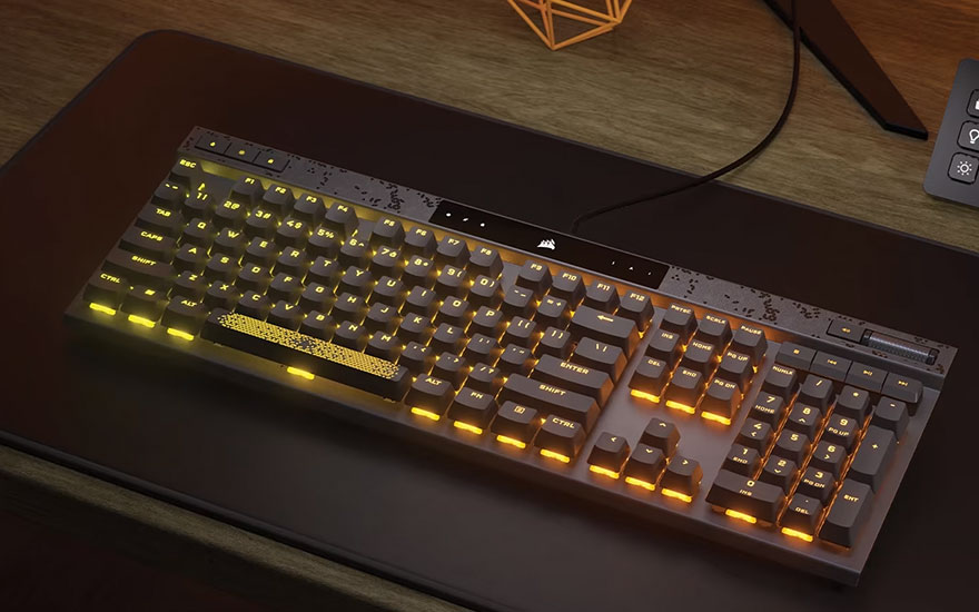 Un clavier noir rétroéclairé en orange est posé sur un tapis de souris noir, sur une table en bois.