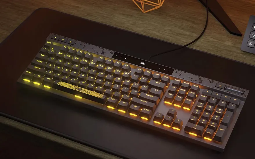 Un clavier noir rétroéclairé en orange est posé sur un tapis de souris noir, sur une table en bois.