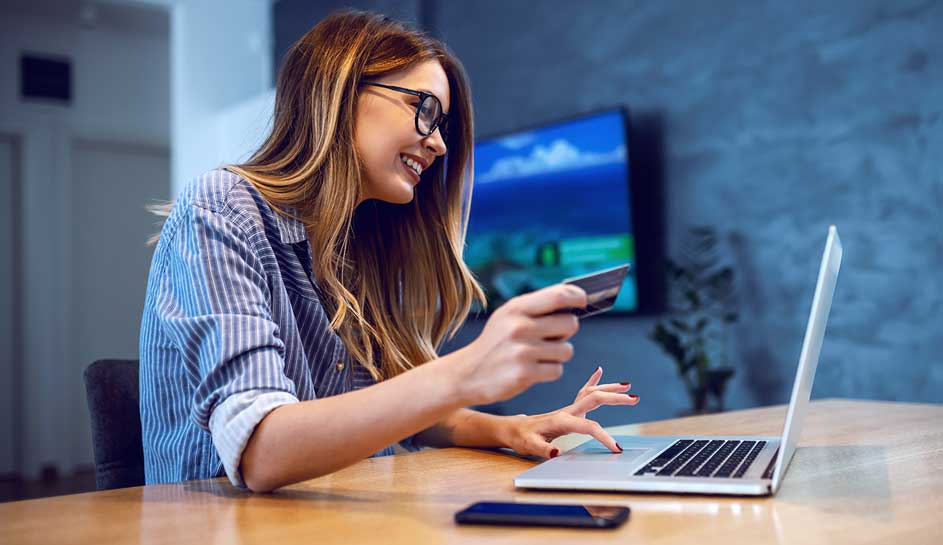 Een laptop en een smartphone liggen op een houten tafel. Een hand houdt een kaart vast. Op de achtergrond een blauwe muur.