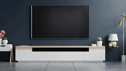Een woonkamer met een grote tv aan een blauwe muur, een tv-meubel, een lamp en decoratie.