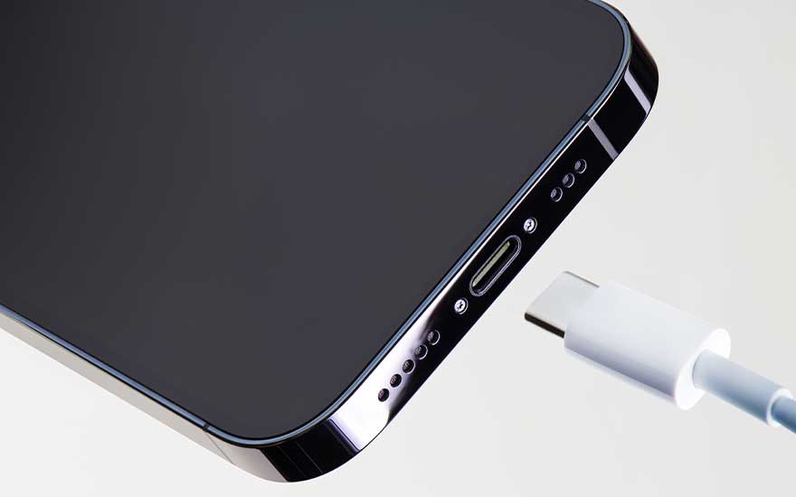 Téléphone noir avec un câble de chargement blanc inséré dans le port. Les boutons et les haut-parleurs sont sur le côté.