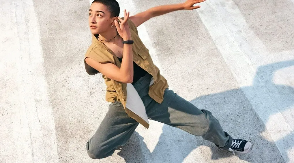 Une personne effectue un mouvement de danse sur une surface en béton avec des lignes blanches. La personne porte un gilet marron.