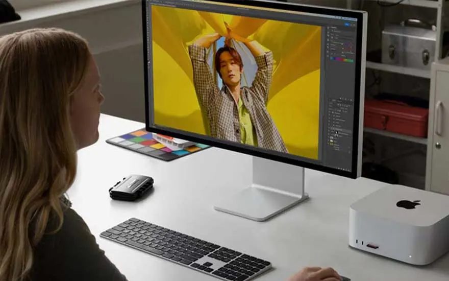 Bureau blanc avec écran affichant une image jaune, clavier, souris et ordinateur Apple. Boîtes de couleur sur le bureau.