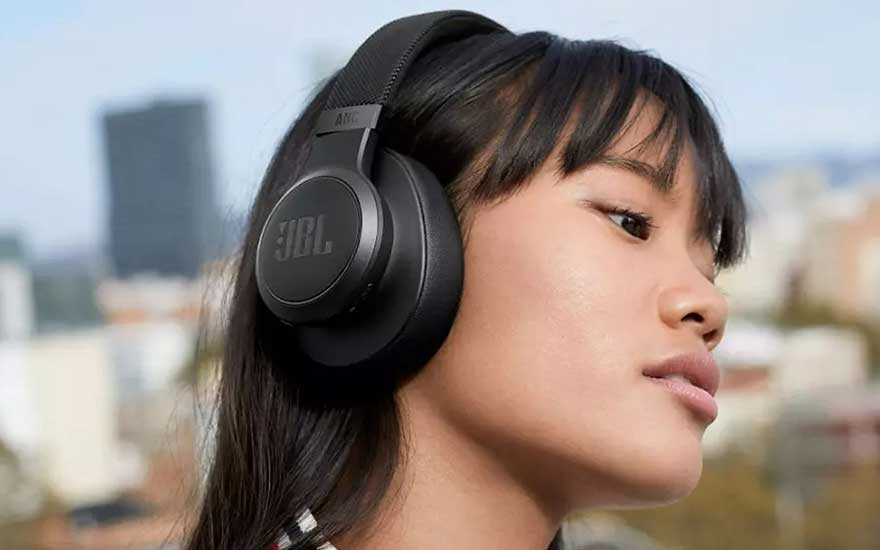 Zwarte JBL-hoofdtelefoon op het hoofd, met vage stadsachtergrond. De focus ligt op de linkeroorschelp.