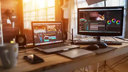 Bureau en bois avec ordinateur portable, écran, clavier et souris affichant un logiciel de montage vidéo. Éclairage vif.