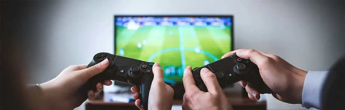 Hands hold black game controllers in front of a screen showing a green field.