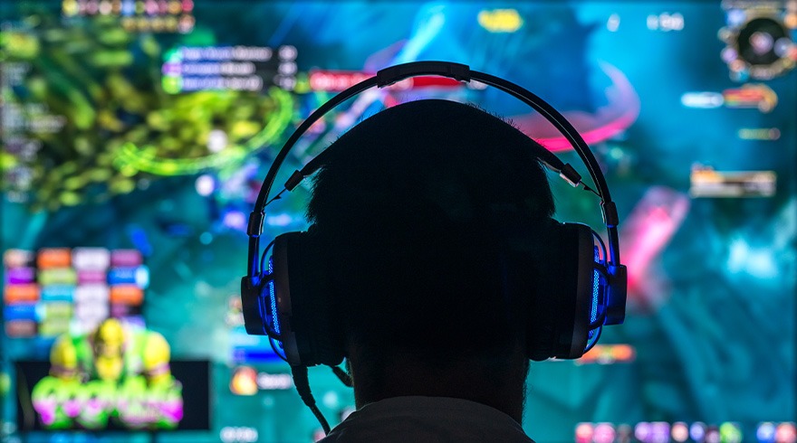 Vue arrière d'une personne portant un casque de jeu bleu devant un écran multicolore affichant un jeu.